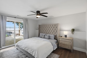 A bedroom with a bed, a nightstand, a ceiling fan, and a view of the outdoors. - Booje Bay : Luxury, Lakefront, Hot Tub! (Sunrise Beach)