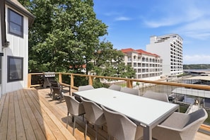 A deck with a table and chairs, overlooking a body of water and buildings. - Booje Bay : Luxury, Lakefront, Hot Tub! (Sunrise Beach)
