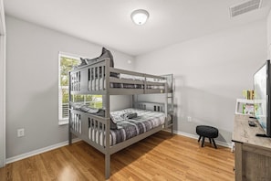 A bunk bed room with a window, a small stool, and a desk with books and a remote control. - 3BR Lakeland Getaway | Pool & AC Game Room (Lakeland)