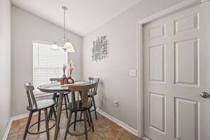 A dining area with a round table, four chairs, a chandelier, and a door. - 3BR Lakeland Getaway | Pool & AC Game Room (Lakeland)