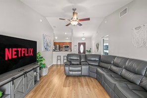 A modern living room with a sectional sofa, a flat-screen TV, and a ceiling fan. - 3BR Lakeland Getaway | Pool & AC Game Room (Lakeland)