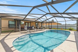 Ein Swimmingpool mit überdachter Terrasse, Liegestühlen und Blick auf ein Gebäude mit Fenster und Tür.