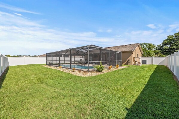 A backyard with a swimming pool, a covered patio area, and a white fence. - 3BR Lakeland Getaway | Pool & AC Game Room (Lakeland)