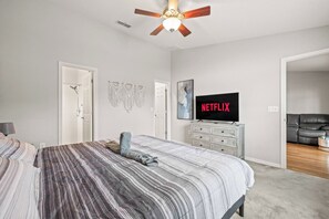 A bedroom with a bed, a ceiling fan, a television displaying 'NETFLIX,' and a door leading to another room. - 3BR Lakeland Getaway | Pool & AC Game Room (Lakeland)