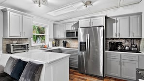 A modern kitchen with stainless steel appliances, white cabinetry, and a central island. - Bradley Beach House by Avantstay Walk to the Beach Hot Tub + Game Room & BBQ Deck (Hilton Head Island)