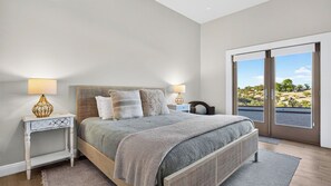 A bedroom with a bed, two bedside tables, a window with a view, and a door. - Vino Vista Villa by Avantstay Pool + Hot Tub Fire Pit + Hammock Hilltop Views Near Downtown (Paso Robles)
