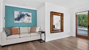 A living room with a teal accent wall, a white sofa with patterned cushions, a wooden side table, and a large mirror. - Vino Vista Villa by Avantstay Pool + Hot Tub Fire Pit + Hammock Hilltop Views Near Downtown (Paso Robles)
