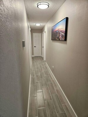 A hallway with a light-colored floor, a door at the end, and a framed picture on the wall. - Spacious Lakeland 4BR | Pool & AC Game Room (Lakeland)