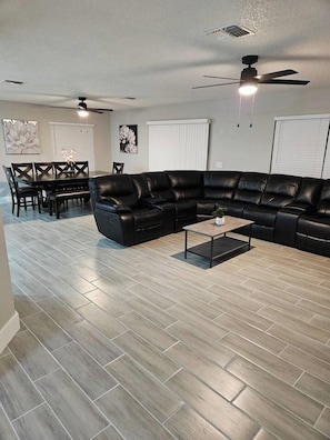 A living room with a sectional sofa, a coffee table, and a dining area with a table and chairs. - Spacious Lakeland 4BR | Pool & AC Game Room (Lakeland)