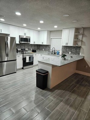 A modern kitchen with white cabinets, stainless steel appliances, and a granite countertop. - Spacious Lakeland 4BR | Pool & AC Game Room (Lakeland)