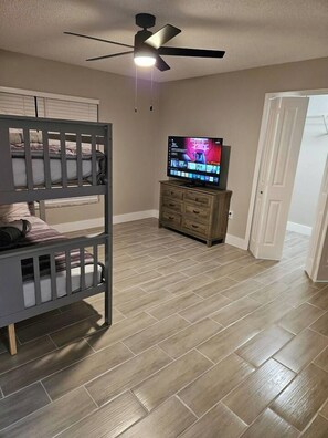 A room with a bunk bed, a television, a wooden cabinet, and a ceiling fan. - Spacious Lakeland 4BR | Pool & AC Game Room (Lakeland)