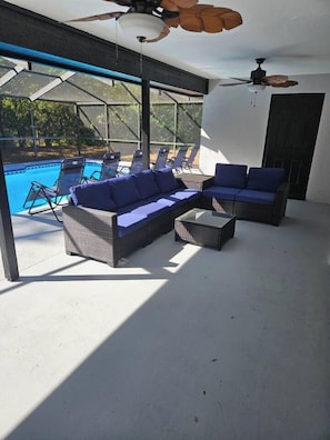 A covered outdoor seating area with wicker furniture and a glass table, overlooking a swimming pool. - Spacious Lakeland 4BR | Pool & AC Game Room (Lakeland)