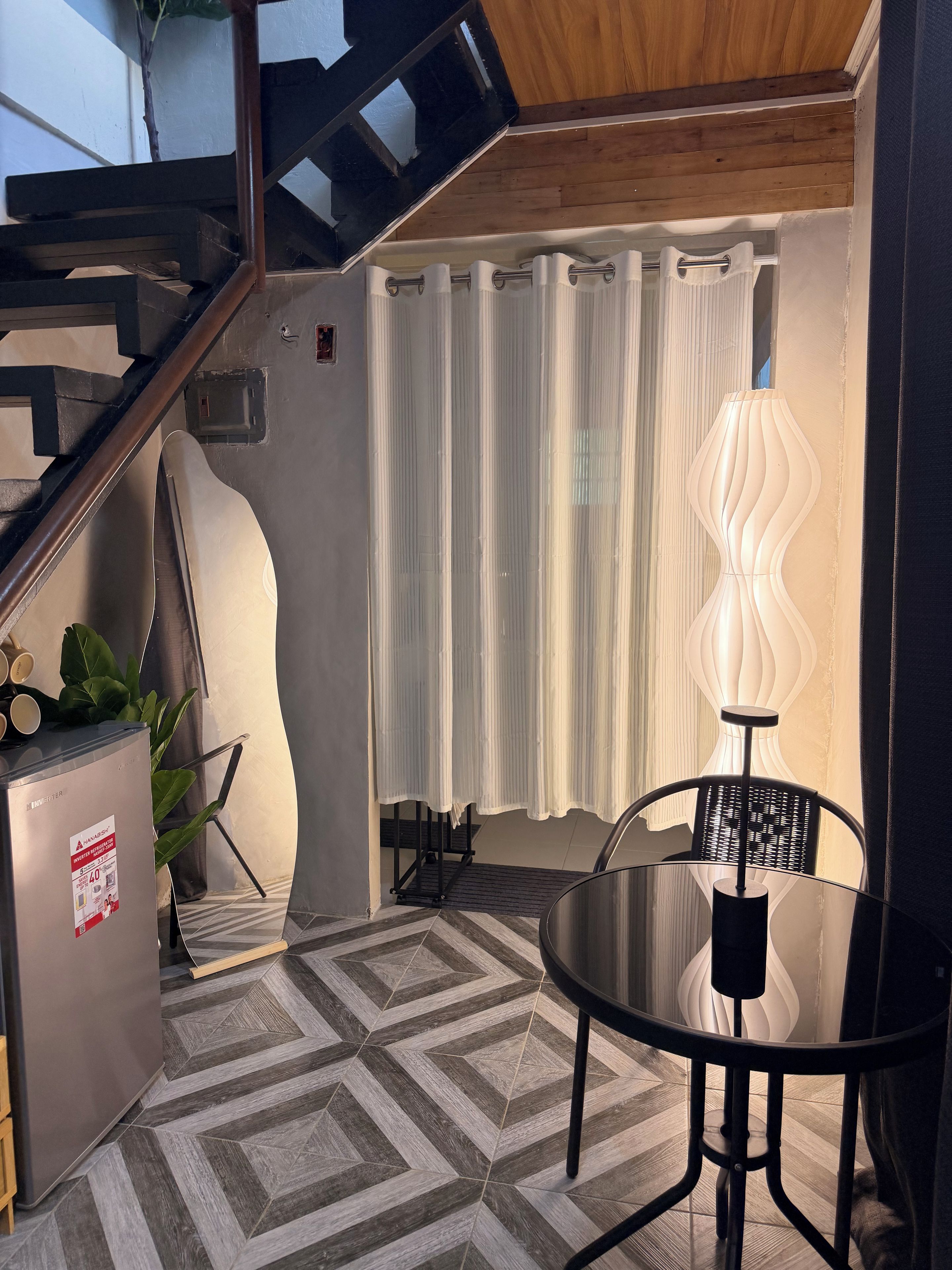 A dining area with a table and chairs, a refrigerator, a potted plant, and a staircase.