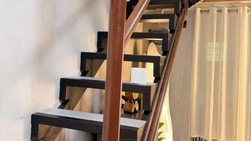 A staircase with wooden steps and metal railings, leading to a room with a patterned floor and a plant in the corner.