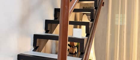 A staircase with wooden steps and metal railings, leading to a room with a patterned floor and a plant in the corner.