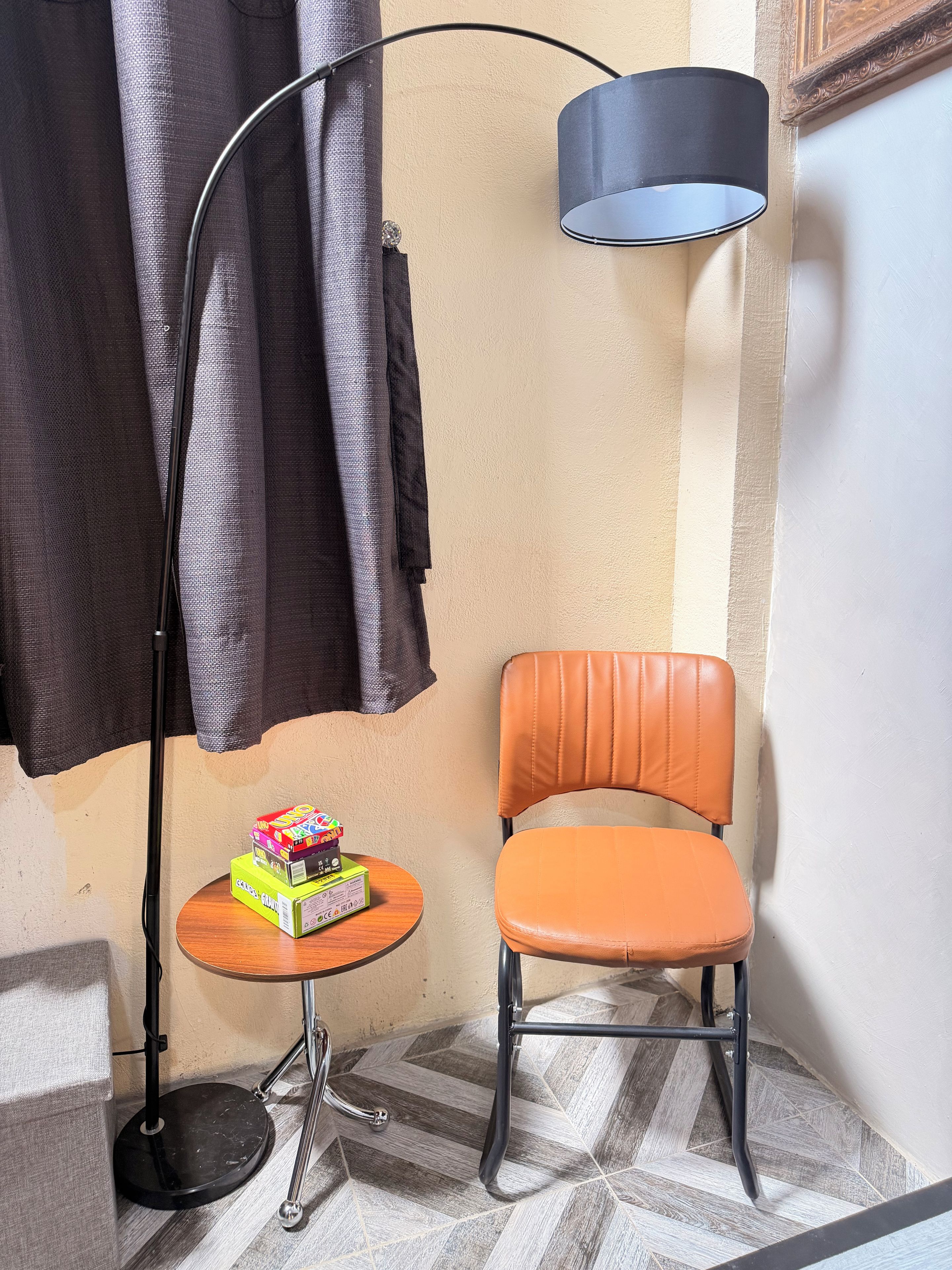 Une pièce d’angle comprenant une chaise, une petite table avec des boîtes, un lampadaire et une lampe fixée au mur.