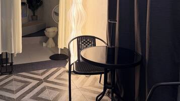 A room with a black metal chair, a small round table, a white floor lamp, and a view of a bathroom through an open door.