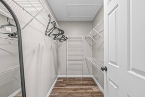 A narrow hallway with wooden flooring, white walls, and metal shelving units on both sides. - Lakeland 3BR | Pool, AC Gameroom & HUGE Yard (Lakeland)