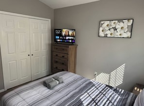 Ein Schlafzimmer mit einem Bett, einem Fernseher auf einem Schrank, einem Kleiderschrank und einem Wandbild.