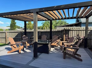 Eine Terrassenanlage im Freien mit einer Pergola, Holzstühlen und einem Tisch mit Glasplatte.