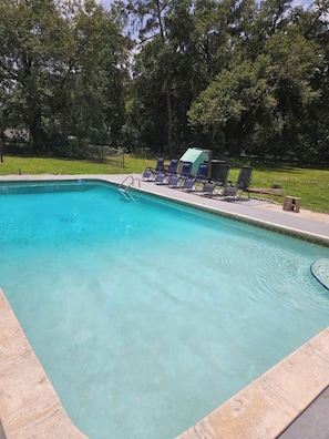 A rectangular swimming pool with a tiled edge, surrounded by a grassy area and trees. - Private Pool • Sleeps 16 • Huge Yard • AC GameRoom (Lakeland)