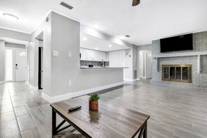 Ampla sala de estar com cozinha, lareira e mesa de jantar com controle remoto.