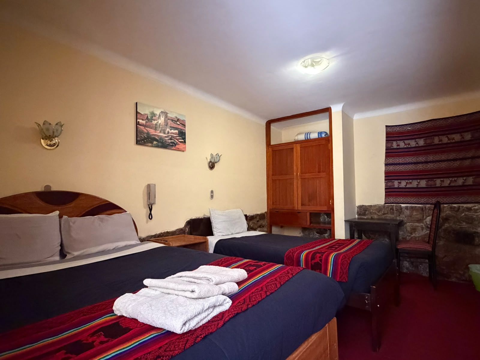 Camera d'albergo con due letti, un armadio in legno, un tavolino, una sedia e un quadro appeso al muro.