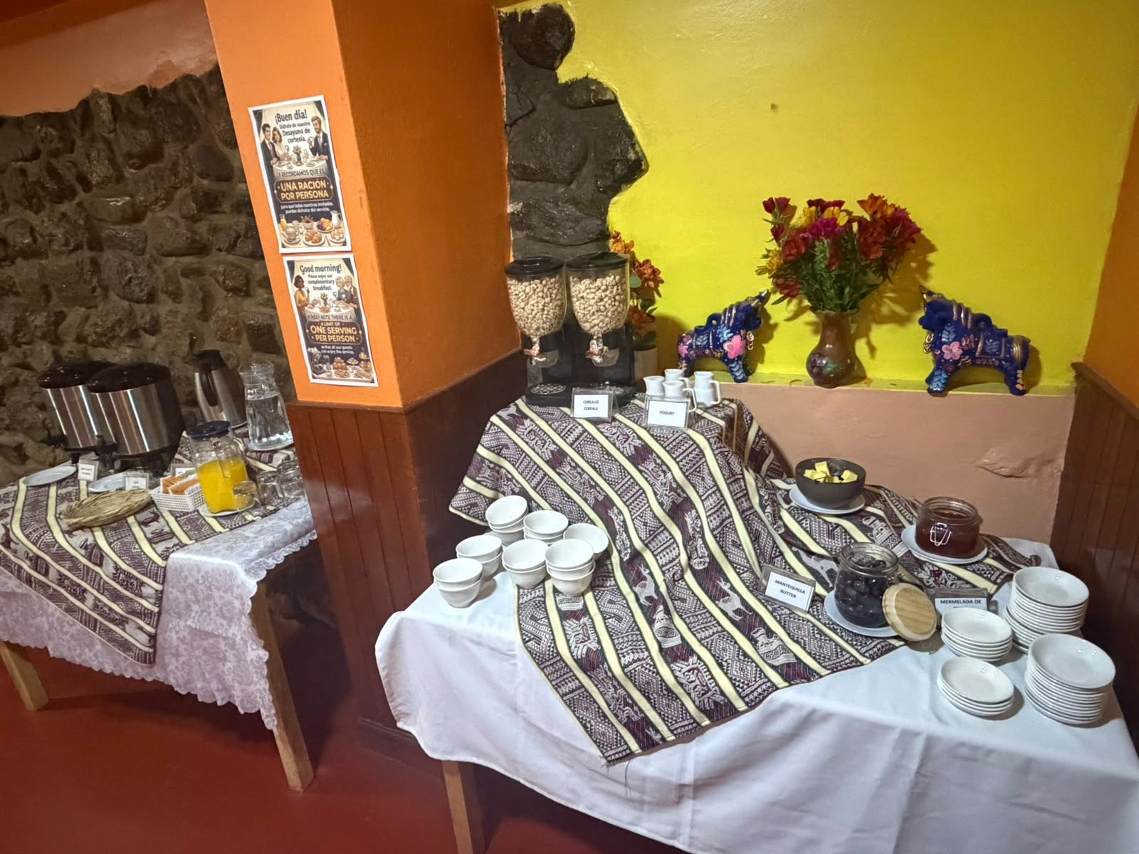 A breakfast buffet setup with a stone wall, a statue, and a yellow wall in the background.
