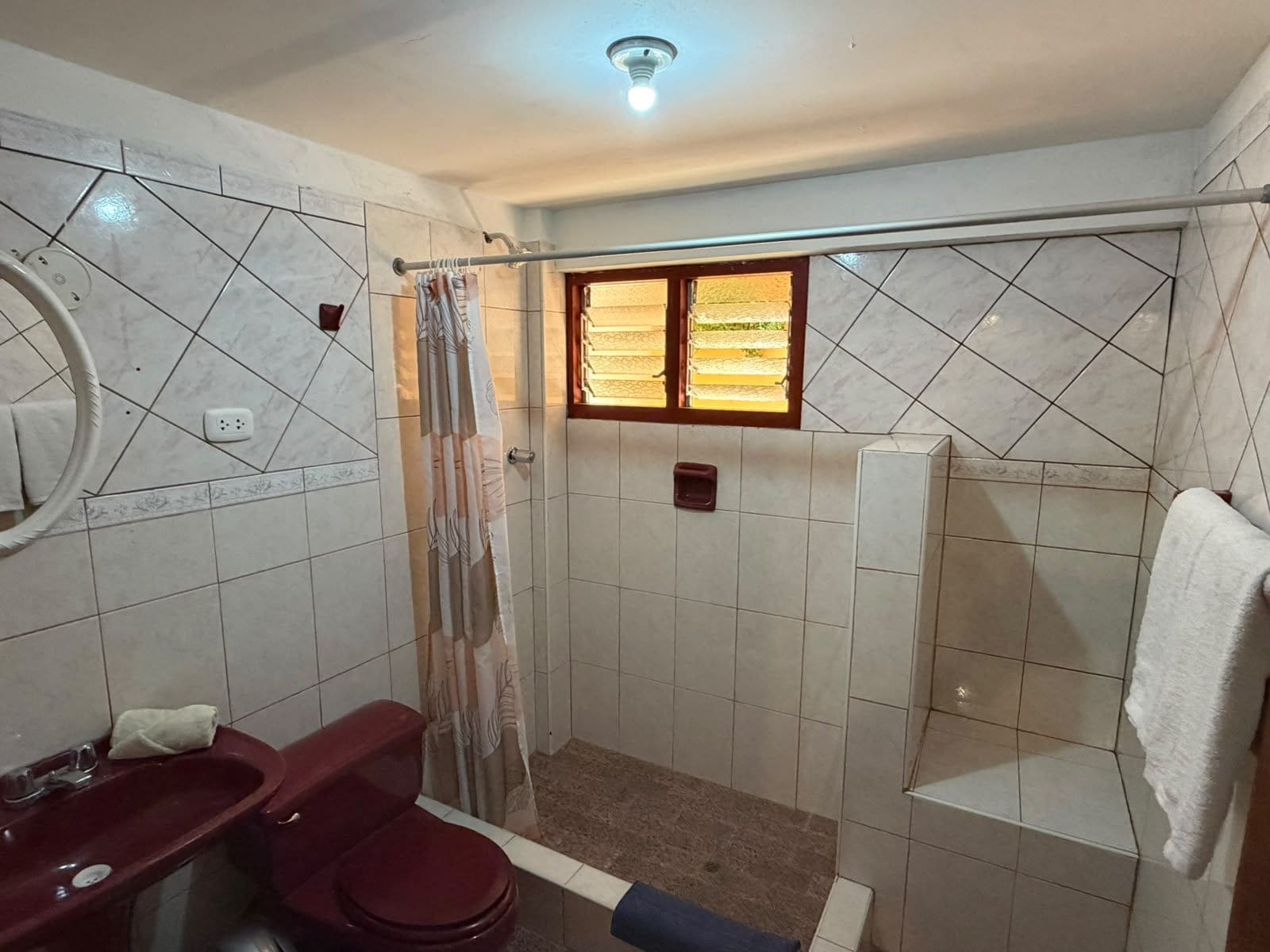 Un bagno con doccia, WC, lavandino e finestra con persiane.