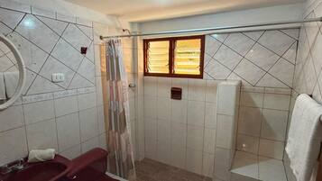 Un bagno con doccia, WC, lavandino e finestra con persiane.
