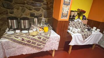 Colazione preparata con due tavoli, ognuno con una caffettiera, una brocca di succo d'arancia e un piatto di cibo.
