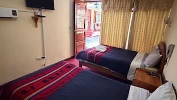 A room with two beds, a television mounted on the wall, and a window with curtains.