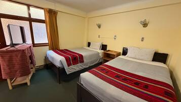 Una camera d'albergo con due letti singoli, un tavolino e una televisione, e una finestra con tende.