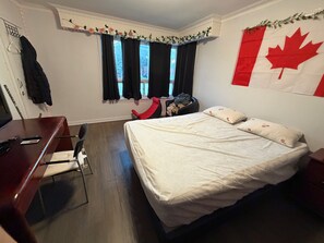 A bedroom with a bed, a desk, a chair, a window with curtains, and a Canadian flag on the wall. - Private room in good location (Toronto)
