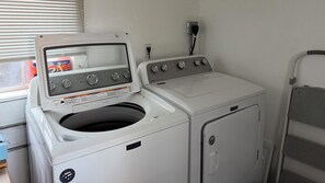 A front-loading washing machine with a control panel, a dryer, and a metal shelf unit. - Comfortable and quirky updated 3-bedroom bungalow in peaceful Monroe (Monroe)