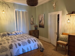 Quarto com cama grande, um banco de madeira, uma cadeira, uma porta e obras de arte na parede.