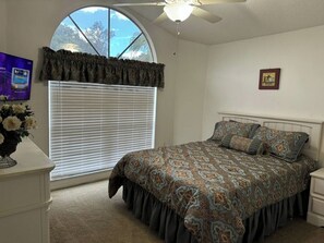 A bedroom with a bed, a window with blinds, a ceiling fan, a nightstand, and a wall-mounted TV. - 3 Bedroom Spacious AC Pool Home w/ Gameroom (Lakeland)