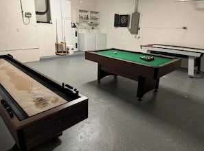 Una sala de billar con dos mesas de billar, un área de lavandería y un dardo.