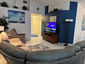 A living room with a sofa, a television on a wooden stand, and a painting on the wall. - 3 Bedroom Spacious AC Pool Home w/ Gameroom (Lakeland)