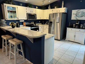 A modern kitchen with a central island, white cabinets, stainless steel appliances, and a blue accent wall. - 3 Bedroom Spacious AC Pool Home w/ Gameroom (Lakeland)