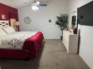 Un dormitorio con cama, cómoda, espejo, ventilador de techo y un reloj de pared.