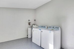 Ein Waschraum mit Waschmaschine und Trockner, einem Warmwasserbereiter und einem an der Wand montierten Wasserspender.