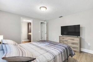 Ein Schlafzimmer mit einem Bett, einer Kommode, einem Fernseher und einer Tür zu einem anderen Raum.