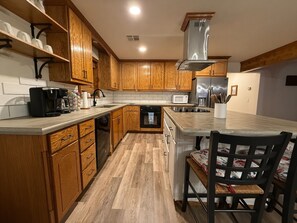 A kitchen with wooden cabinets, a microwave, a coffee maker, and a dining area with a table and chairs. - Pop’s Place at Blackgum - near Lake Tenkiller, sleeps 8-10, handicap accessible (Vian)