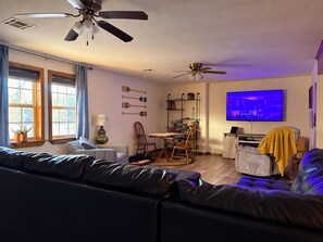 A living room with a sofa, a dining table, chairs, a TV, and ceiling fans. - Pop’s Place at Blackgum - near Lake Tenkiller, sleeps 8-10, handicap accessible (Vian)