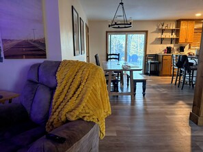 Een woonkamer met een bank, een eettafel en een keuken op de achtergrond.