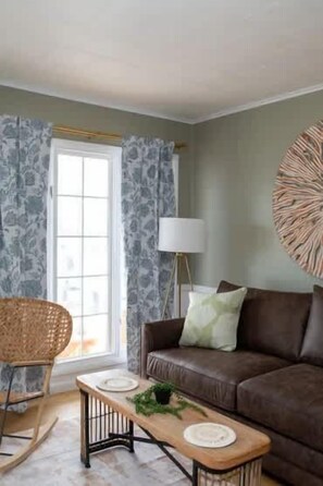 A living room with a brown sofa, a wooden coffee table, a wicker chair, and a floor lamp. - Sunset Cove & Drift Inn 2BD | Waterfront Getaway (Berlin)