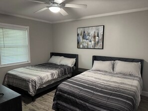 A bedroom with two beds, a ceiling fan, a window with blinds, and a cityscape painting on the wall. - 4 Bedroom Cul-de-Sac Pool Home w/ Gameroom (Lakeland)
