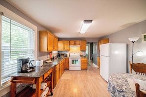 A compact kitchen with wooden cabinets, a white refrigerator, and a dining area with a patterned tablecloth. - The Rain Dancer Art House. (Paducah)