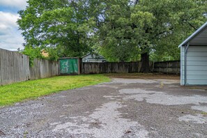 Une allée de gravier mène à une clôture en bois, à un abri de jardin vert et à une maison avec un garage.